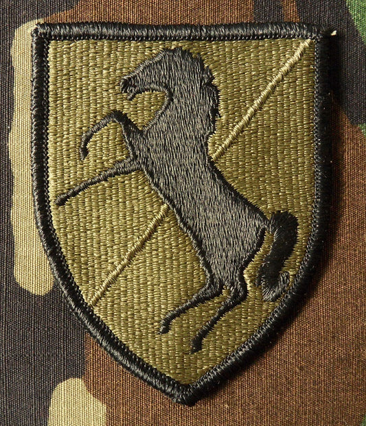 Schildförmiges Patch des 11th Armored Cavalry Regiment der US-Armee olivgrün mit einem springenden schwarzen Pferd in der Mitte