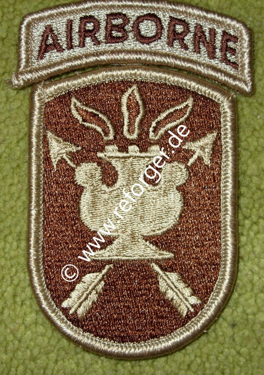 Schildförmiges Patch des JFK Special Warfare Center der US-Armee in Beige und Braun, mit einer antiken Lampe in der Mitte, die von zwei gekreuzten Pfeilen durchzogen wird